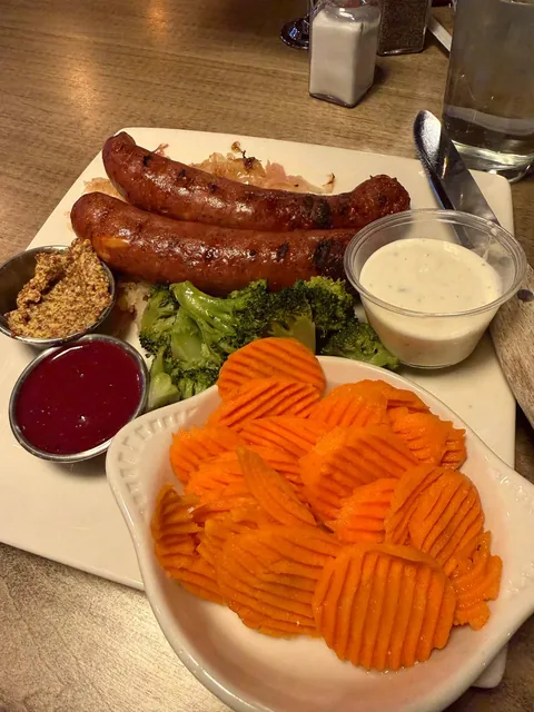 A Zwickel plate before eating: two grilled sausages on kraut with broccoli, a bowl of crinkle-cut carrot chips and three small sauce cups.